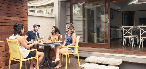 Group Of Four Young Adults Relaxing On Patio Outside House With Food And Drink