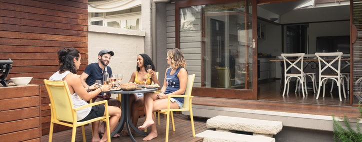 Group Of Four Young Adults Relaxing On Patio Outside House With Food And Drink