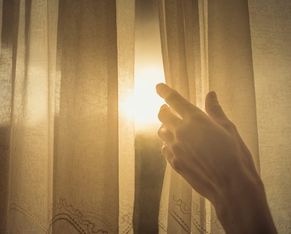 Hand opening up window curtain letting the early morning sunshine in.