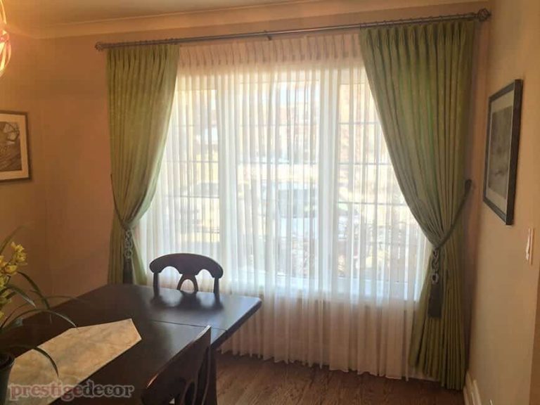 Green pattern curtains with tiebacks, sheers and iron decorative drapery hardware in a dining room.