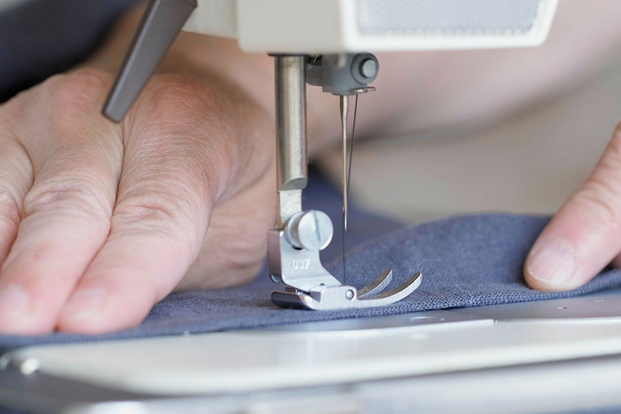 Hands of seamstress sewing with a professional machine, embroiders sews on grey fabric.