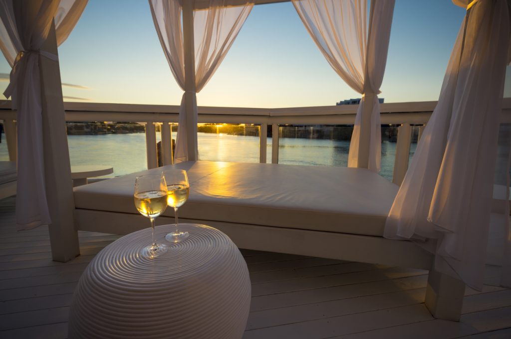 Two glasses of white wine beside day bed at sunset.