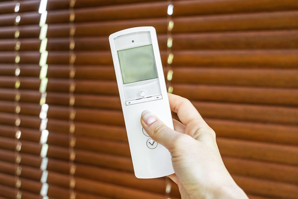 female hand holds a remote control to open the window blinds